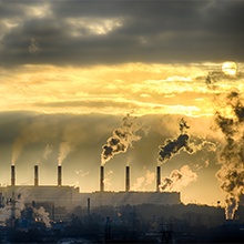 Factories belch pollution into a hazy sky as the sun peaks out from behind the clouds.